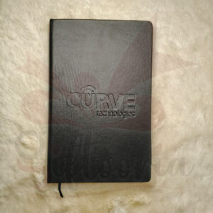 Close-up of a black faux leather diary with a subtle debossed/embossed logo placeholder on the cover, resting on a fuzzy white surface