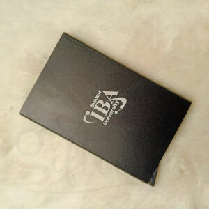 Close-up of a rectangular black metal pop-up card holder with a matte finish, designed for business and credit cards, resting on a soft white fabric.