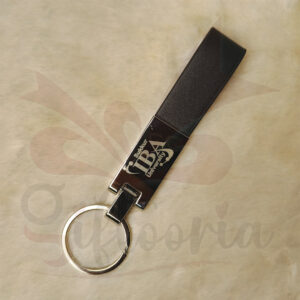 A black leather strap keychain with a silver metal section, attached to a silver split key ring, resting on a fuzzy white surface.
